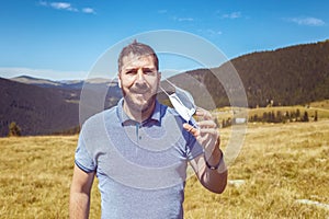 Portrait of mature man taking off protective face mask and breathing fresh air on top of the mountains