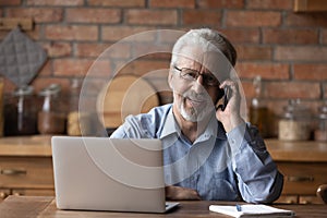 Portrait of mature man talk on smartphone working on laptop