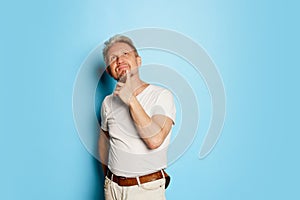 Portrait of mature man in white T-shirt posing  over blue studio background. Thoughful face