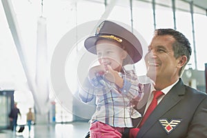 Portrait of mature pilot carrying cute little child in airport