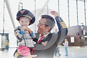 Portrait of mature pilot carrying cute little child in airport