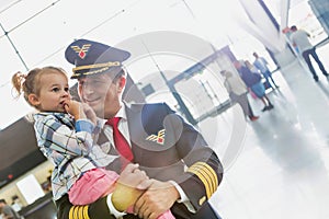 Portrait of mature pilot carrying cute little child in airport