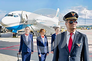 Portrait of mature pilot walking with three young beautiful flight attendants against airplane in airport