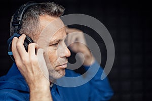 Portrait of mature radio host putting on headphones during making podcast