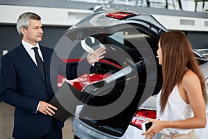 Portrait of mature sales manager sitting across desk in car dealership showroom, copy space