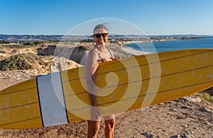 Portrait of mature senior Surfer looking at the ocean with vintage surfboard on an empty beach