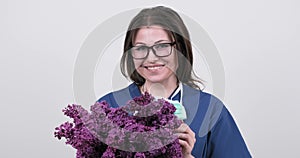 Portrait of mature smiling female doctor in glasses with protective medical mask holding bouquet of flowers