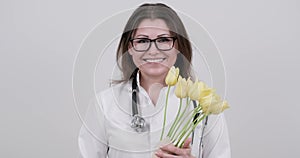 Portrait of mature smiling female doctor in glasses with stethoscope holding bouquet of flowers