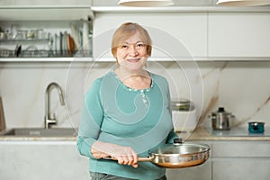 Portrait of a mature smiling woman with a frying pan in her hands