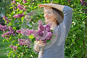 Portrait of mature smiling woman in garden with bouquet of lilacs