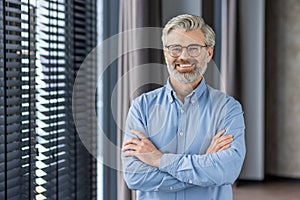 Portrait of mature successful businessman boss, senior gray-haired man inside office smiling looking at camera with