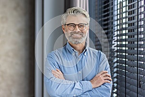 Portrait of mature successful businessman boss, senior gray-haired man inside office smiling looking at camera with