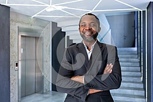Portrait of mature and successful businessman inside office, boss smiling and looking at camera with crossed arms