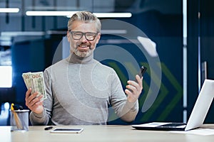 Portrait of mature successful businessman inside office, senior gray haired man smiling and looking at camera, investor