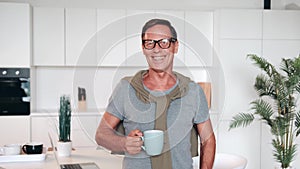 portrait of a mature successful man looking at the camera and smiling and holding a cup of coffee or tea in his hands
