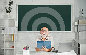 Portrait of mature teacher or tutor professor working at table in college or high school. Adult teaching.