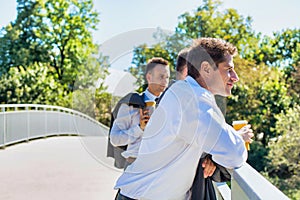 Portrait of mature thoughtful attractive businessman drinking coffee while standing on the bridge with colleagues