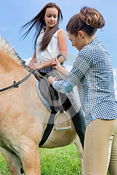 Portrait of mature woman adjusting leathers on horse for stirrup iron in ranch photo