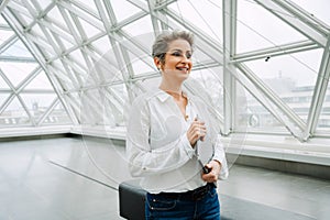 Portrait of mature woman art gallery manager holding laptop while standing in museum