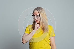 Portrait of mature woman in glasses keeping finger at her mouth, saying Shh, Hush, Tsss. Silence and secret concept photo