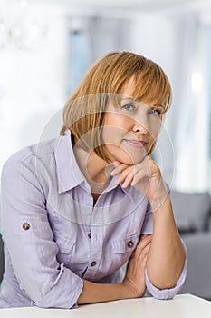 Portrait of mature woman with hand on chin sitting at table in house