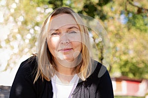 Portrait of a mature woman looking at the camera. Relaxed look of a happy, smiling woman outdoors. Warm, sunny day. Blurred