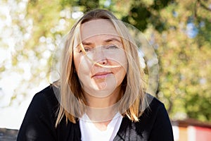 Portrait of a mature woman looking at the camera. Relaxed look of woman in outdoors. A strand of hair lies on the face. Warm,