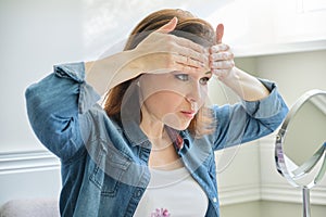 Portrait of mature woman with make-up mirror massaging her face