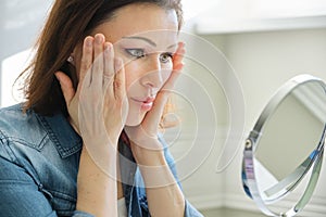 Portrait of mature woman with make-up mirror massaging her face
