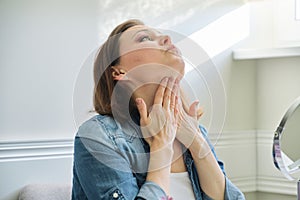 Portrait of mature woman with make-up mirror massaging her face and neck