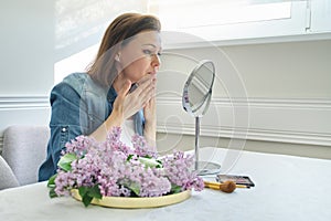 Portrait of mature woman with make-up mirror massaging her face and neck, beautiful female 40 years old