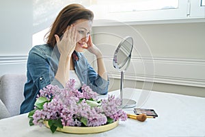 Portrait of mature woman with make-up mirror massaging her face and neck, beautiful female 40 years old