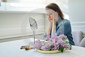 Portrait of mature woman with make-up mirror massaging her face and neck, beautiful female 40 years old