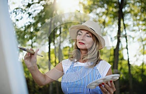 Portrait of mature woman with pallete painting outdoors in garden.