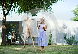 Portrait of mature woman with pallete painting outdoors in garden.