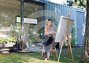 Portrait of mature woman with pallete painting outdoors in garden.