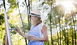 Portrait of mature woman with pallete painting outdoors in garden.