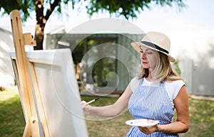 Portrait of mature woman with pallete painting outdoors in garden.