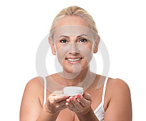 Portrait of  mature woman with perfect skin holding jar of cream on white background