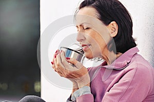 Portrait of mature woman resting after jog in the park with cup of hot tea