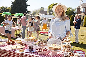 Portrait Of Mature Woman Serving On Cake Stall At Busy Summer Garden Fete