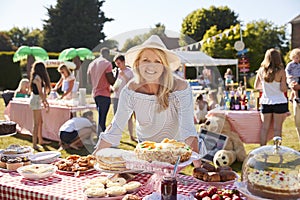 Portrait Of Mature Woman Serving On Cake Stall At Busy Summer Garden Fete