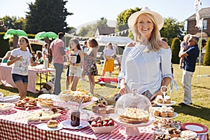 Portrait Of Mature Woman Serving On Cake Stall At Busy Summer Garden Fete photo