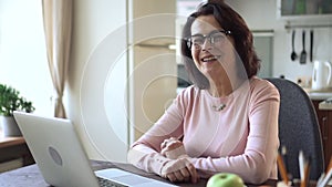 Portrait of mature woman sit at kitchen with laptop. Retired old female finish typing on keyboard