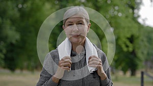 Portrait of the mature woman in sporty clothes carrying a towel in her neck. standing in park. Elderly female athlete