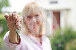 Portrait Of Mature Woman Standing In Garden In Front Of Dream Home In Countryside Holding Keys