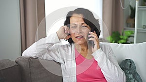 Portrait of mature woman talking phone sitting on sofa in home room.
