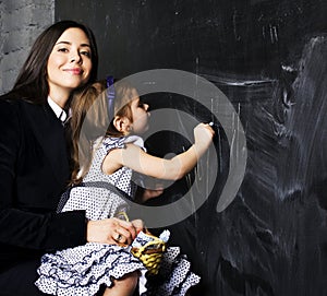 Portrait of mature woman teacher with little cute blonde girl pupil writing on blackboard together, lifestyle people