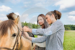 Portrait of mature woman teaching young woman on how to pull horse bit