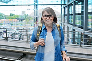 Portrait of mature woman at train station, female with backpack looking at camera